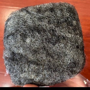 May include: A close-up of a black and grey hairpiece. The hair is curly and textured.