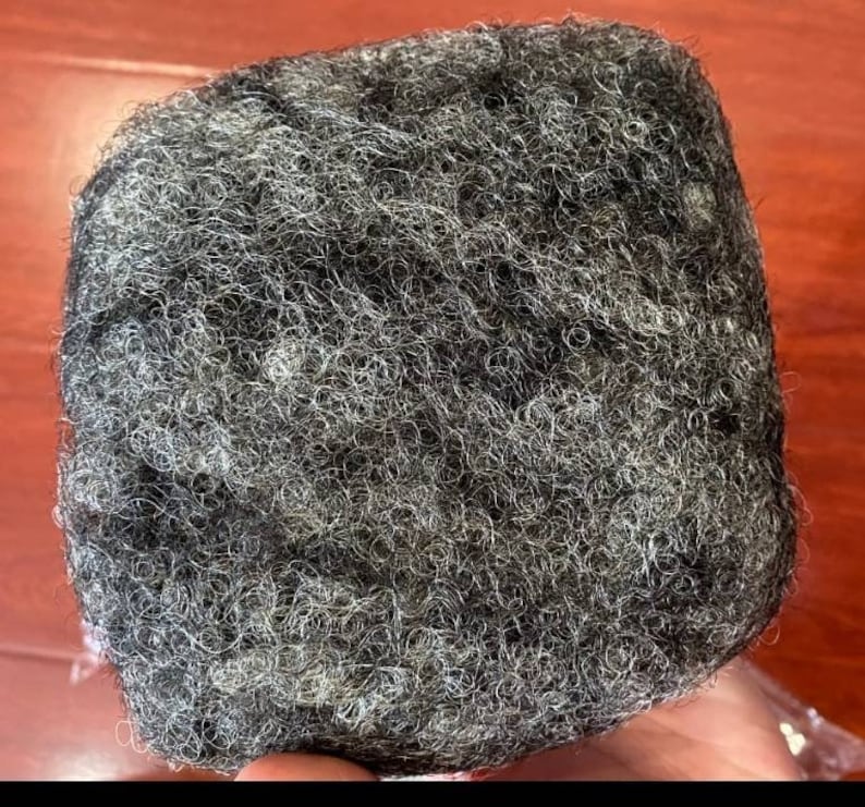 May include: A close-up of a black and grey hairpiece. The hair is curly and textured.