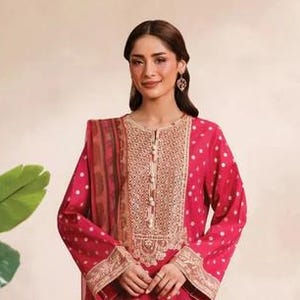 May include: A magenta-colored, long-sleeved tunic and matching dupatta with white polka dots. The tunic features gold embroidery around the neckline and cuffs. The ensemble is paired with floral print pants, creating a coordinated outfit.