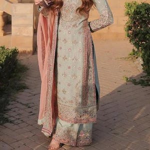 K&ouml;nnte beinhalten: Ein hellblaues Set aus lang&auml;rmeliger Tunika und weit geschnittener Hose mit aufwendiger silberner und rosafarbener Blumenstickerei, kombiniert mit einem passenden hellblauen Dupatta mit rosa Rand, verziert mit zarten Pailletten und Stickereien.