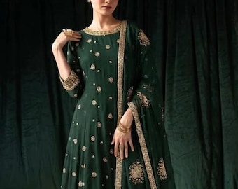Könnte beinhalten: Ein dunkel smaragdgrüner Anarkali-Anzug bestehend aus einem langärmeligen Kurta mit goldener Blumenstickerei, einer passenden Hose mit geradem Bein und einem transparenten Dupatta mit breitem Goldrand und goldenen Blumenmotiven.