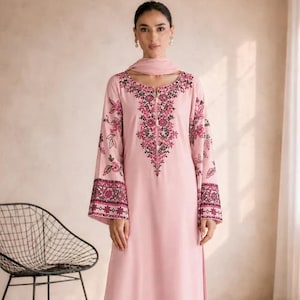 May include: A light pink long-sleeved tunic and wide-leg trousers set featuring intricate dark pink and black floral embroidery along the neckline, sleeve cuffs, and pant hems, accompanied by a matching light pink scarf draped around the neck.
