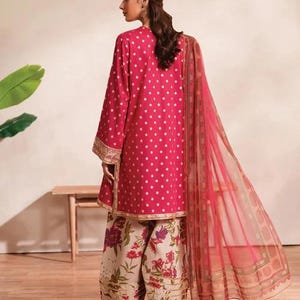 May include: A magenta polka-dot tunic with long sleeves and gold trim, paired with floral print pants and a sheer scarf. The outfit is part of a traditional South Asian ensemble, showcasing a blend of patterns and colors.