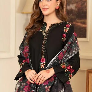 May include: Black embroidered tunic and shawl set. The tunic features floral embroidery in pink, red, and gold around the neckline and sleeves. The shawl has a floral pattern in pink, red, and green. The outfit is a traditional style.
