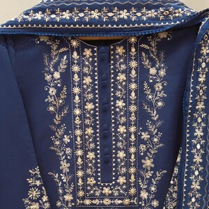 May include: A navy blue embroidered outfit featuring intricate gold floral patterns. The ensemble includes a tunic with a button-down front and a matching scarf, all adorned with detailed embroidery. The design is elegant and suitable for special occasions.