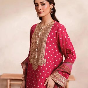 May include: A magenta-colored, long-sleeved tunic with white polka dots. The tunic features an ornate gold embroidered neckline and cuffs, with pearl-like buttons. The sleeves have a patterned border. The outfit is suitable for special occasions.