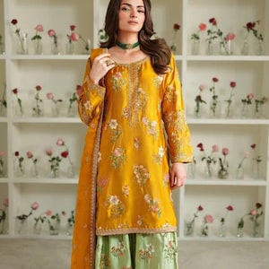 May include: Mustard yellow embroidered tunic and matching scarf paired with light green palazzo pants. The floral embroidery features pink and white flowers. The outfit is worn by a person in front of a wall of roses.