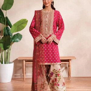 May include: A magenta-colored, long-sleeved tunic and matching dupatta with white polka dots. The tunic features gold embroidery around the neckline and cuffs. The ensemble is paired with floral print pants, creating a coordinated outfit.