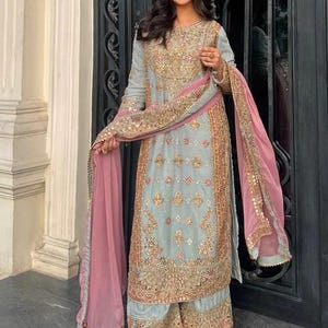 K&ouml;nnte beinhalten: Ein hellblaues Set aus lang&auml;rmeliger Tunika und weit geschnittener Hose mit aufwendigen Goldstickereien, Pailletten und Perlenarbeiten. Das Ensemble enth&auml;lt einen passenden hellblauen Dupatta mit rosa Rand und Goldbesatz &uuml;ber den Schultern.