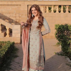 K&ouml;nnte beinhalten: Ein hellblaues Set aus lang&auml;rmeliger Tunika und weit geschnittener Hose mit aufwendiger silberner und rosafarbener Blumenstickerei, kombiniert mit einem passenden hellblauen Dupatta mit rosa Rand, verziert mit zarten Pailletten und Stickereien.