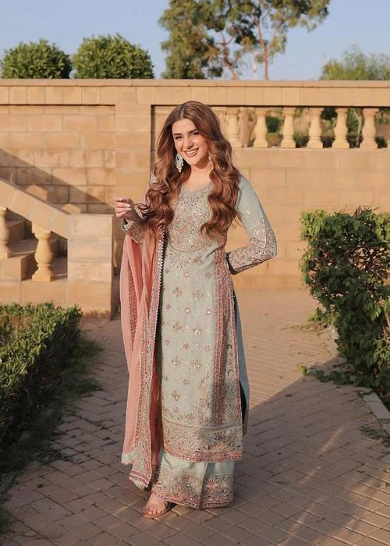 K&ouml;nnte beinhalten: Ein hellblaues Set aus lang&auml;rmeliger Tunika und weit geschnittener Hose mit aufwendiger silberner und rosafarbener Blumenstickerei, kombiniert mit einem passenden hellblauen Dupatta mit rosa Rand, verziert mit zarten Pailletten und Stickereien.