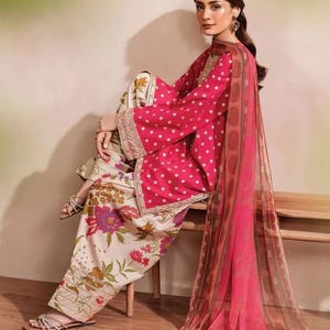 May include: A woman's ensemble featuring a pink polka-dot top with wide sleeves, paired with floral print pants. A matching sheer scarf drapes over the shoulder. The outfit is accented with gold trim.