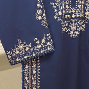 May include: A navy blue garment with intricate gold floral embroidery. The embroidery adorns the neckline, sleeves, and a vertical panel, creating a detailed and elegant design. The sleeves have a delicate trim.