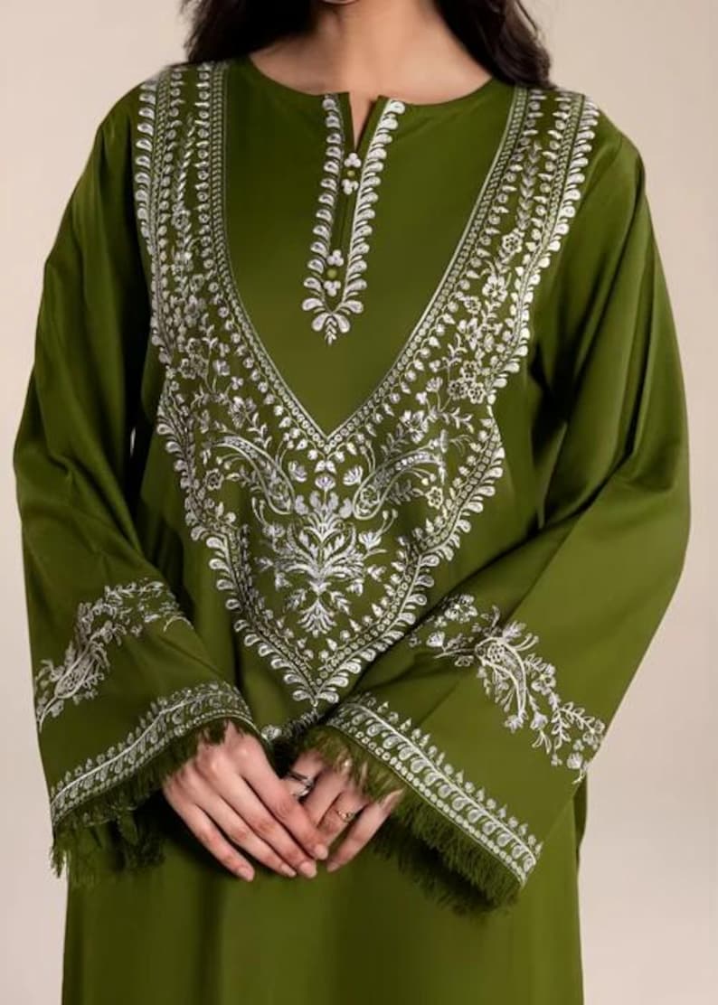May include: Olive green tunic with long sleeves and intricate white floral embroidery. The embroidery frames the neckline and adorns the cuffs, which are finished with a fringe. A stylish, elegant top.