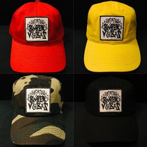 May include: Four baseball caps with a black and white logo that says "Dark Vibes" on the front. The caps are red, yellow, camouflage, and black.