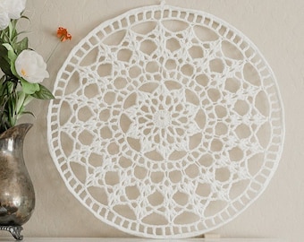 May include: White crocheted wall hanging with a circular design featuring a large star in the center. The design is intricate and delicate, with a repeating pattern of smaller stars.
