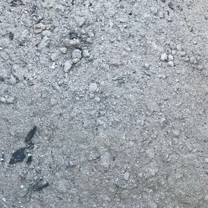 May include: Close-up of a pile of gray gravel with small black pieces of charcoal mixed in.
