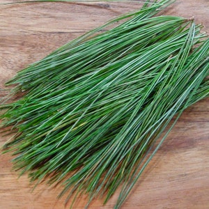 May include: A bunch of long, thin, green pine needles on a wooden surface.