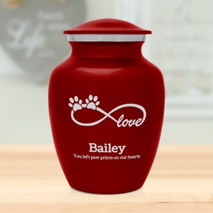 May include: Red pet cremation urn with a white infinity symbol and the word "love" inside. The urn also has two paw prints and the name "Bailey" with the text "You left paw prints on our hearts".