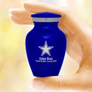 May include: A small blue cremation urn with a silver lid. The urn has a white star and the text "Jake Sun August 20, 1957 - June 22, 2020" engraved on it.