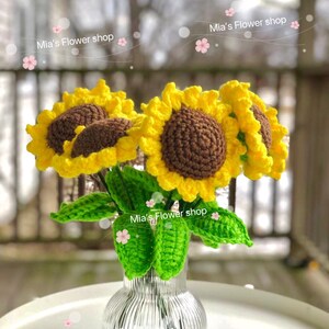 Peut inclure: Un bouquet de tournesols en crochet dans un vase en verre transparent &agrave; texture c&ocirc;tel&eacute;e. Les tournesols sont jaunes avec des centres bruns et des feuilles vertes. Le vase est pos&eacute; sur une table blanche. Le texte "Mia's Flower shop" appara&icirc;t plusieurs fois dans l'image.