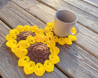 May include: Three crocheted sunflower coasters in yellow and brown, with a white ceramic mug sitting on one of the coasters.