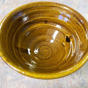 May include: A brown ceramic bowl with a glossy finish. The bowl has a slightly rounded shape and a wide rim.