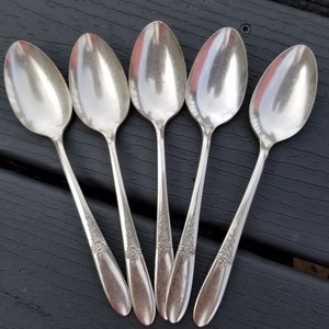 Peut inclure: Cinq cuillères en argent avec des motifs ornés sur les manches. Les cuillères sont disposées en éventail sur une surface noire.