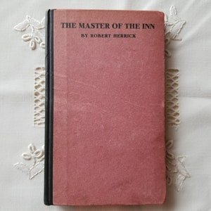 Pode incluir: Um livro encadernado em vermelho com o título "The Master of the Inn" de Robert Herrick.