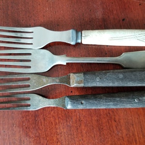 May include: Four forks with different handles. The top fork has a white wooden handle, the second fork has a silver handle, the third fork has a dark brown wooden handle, and the bottom fork has a black wooden handle.