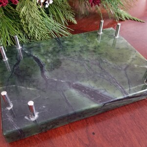 May include: A green marble base with silver metal accents. The base has a smooth, polished surface and a rectangular shape.