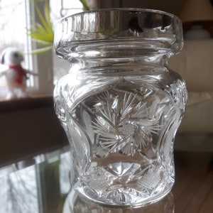 Könnte beinhalten: Eine klare Glasvase mit einem dekorativen geschliffenen Glasdesign. Die Vase hat eine breite Öffnung und einen Deckel.