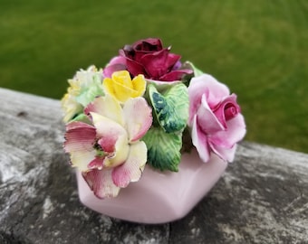 Könnte beinhalten: Eine rosa Porzellanvase mit einem Blumenstrauß. Die Blumen sind ein Mix aus rosa, gelben und roten Rosen und grünen Blättern.
