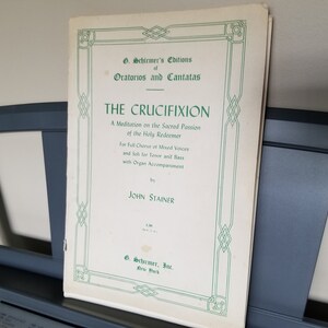 Puede incluir: Una portada de partitura blanca con un borde verde. El título es "The Crucifixion" de John Stainer. Es una meditación sobre la pasión sagrada del Santo Redentor para coro completo de voces mixtas y soli para tenor y bajo con acompañamiento de órgano.