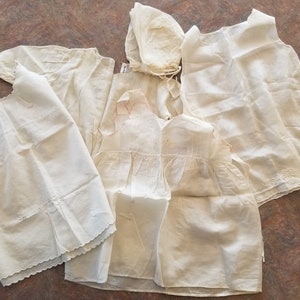 May include: Five white cotton baby dresses with lace trim and embroidery. The dresses are vintage and have a delicate, feminine look.