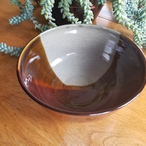 May include: A large, brown and white ceramic bowl with a glazed finish. The bowl has a wide, rounded shape and a smooth, even surface.