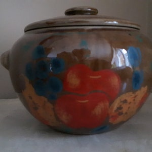 May include: A brown ceramic crock with a lid, featuring hand-painted fruit and grape designs in shades of red, orange, blue, and yellow.