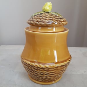 Peut inclure: Un pot en céramique avec un couvercle en forme de panier surmonté d'une poire. Le pot est brun et présente un motif tissé. Le couvercle est brun et vert.