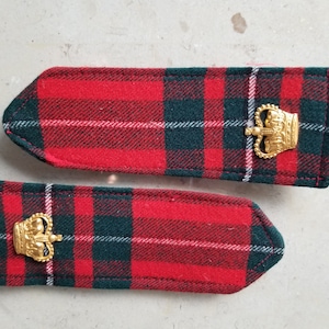 May include: Two red and green plaid fabric patches with gold crown embellishments. The patches are rectangular with rounded corners.