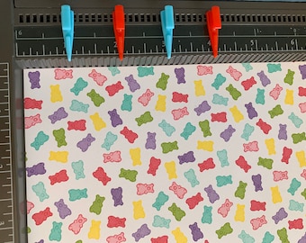 Puede incluir: Una hoja de papel blanco con un patrón repetido de ilustraciones de ositos de goma de colores.