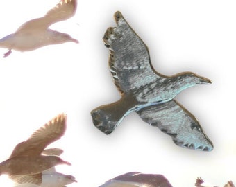 May include: A flock of seagulls in flight over a body of water. The seagulls are white with grey wings and some have brown markings. The water is blue and there is a bright sun reflecting off the water.