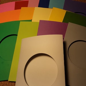 May include: A stack of colorful cardstock paper with a circular cut-out in each sheet. The colors include pink, red, orange, yellow, green, purple, blue, and gray.