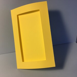 May include: A yellow frame with a curved edge and a rectangular opening. The frame is made of a thick, sturdy material.