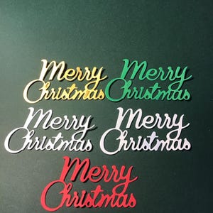 May include: Five cut-out Christmas greetings in gold, green, white, and red script. The words "Merry Christmas" are displayed in a cursive font against a dark green background. Festive holiday decor.