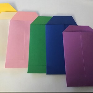 May include: A set of six envelopes in different colors, including yellow, cream, pink, green, blue, and purple. The envelopes are all the same size and shape, and they are arranged in a row from left to right.