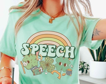 May include: A heather mint green t-shirt with a rainbow and the word "SPEECH" in a retro font. The design also includes shamrocks, a horseshoe, a pot of gold, and a bingo card.