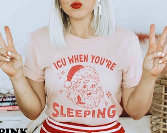 Könnte beinhalten: Hellrosa T-Shirt mit dem Text "ICU WHEN YOU'RE SLEEPING" und einer Weihnachtsmann-Grafik. Das Model trägt rot-weiß gestreifte Shorts und ein rot-weißes Stirnband. Das Wort "PINK" befindet sich unten links im Bild.