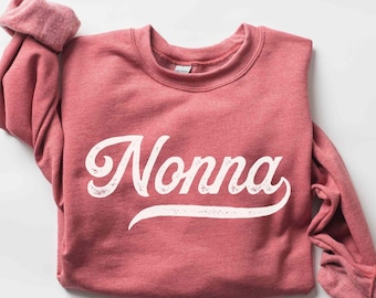 Könnte beinhalten: Heather-scharlachroter Sweatshirt mit dem Wort "Nonna" in weißer Vintage-Schrift gedruckt.