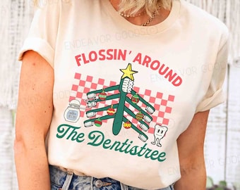 May include: A cream-coloured t-shirt with a dental-themed graphic. The design features a Christmas tree made of toothbrushes, ornaments, and a star, with the text "FLOSSIN' AROUND The Dentistree" in red and green.