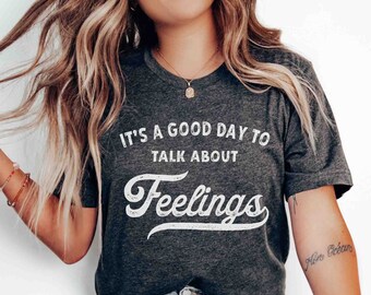 May include: A dark grey t-shirt with white text that reads "It's a good day to talk about feelings". The text is in a vintage style font.